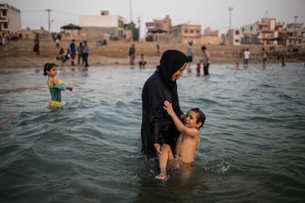 Женщина купает ребенка в Персидском заливе в городе Бушер
