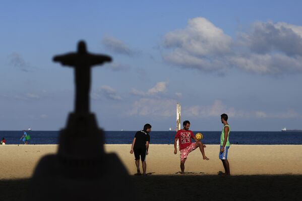 Миниатюрная копия статуи Христа-Искупителя на фоне играющих в алтиньо людей на пляже в Рио-де-Жанейро