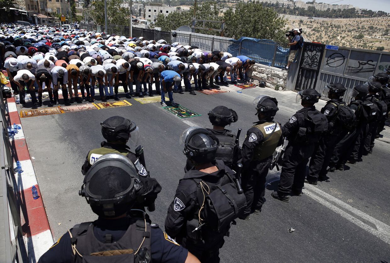 Израильские полицейские смотрят на палестинцев, молящихся в первую пятницу священного месяца Рамадан