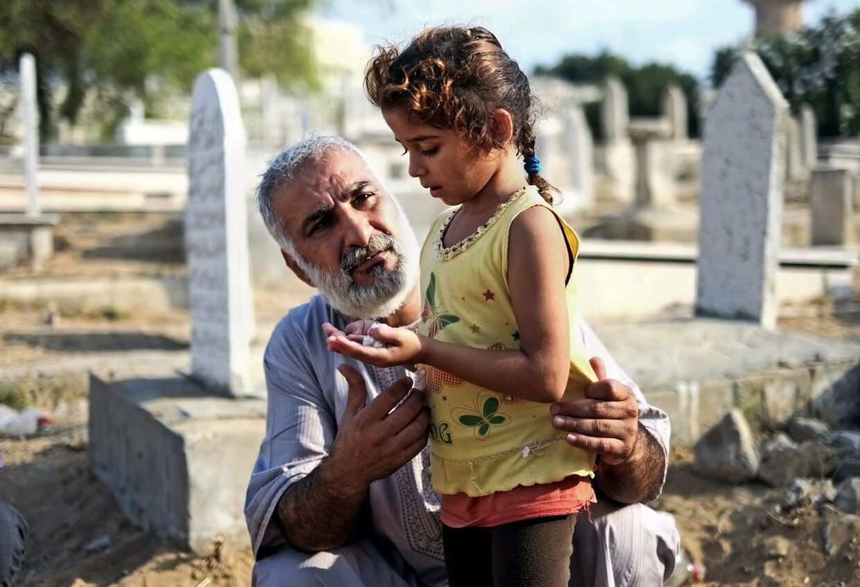 Мужчина и девочка молятся на кладбище в городе Газа во время праздника Ид аль-Фитр