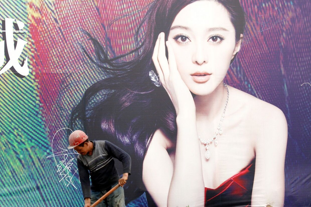 Рабочий-мигрант на фоне плаката с портретом актрисы Фань Бинбин в городе Сянъян