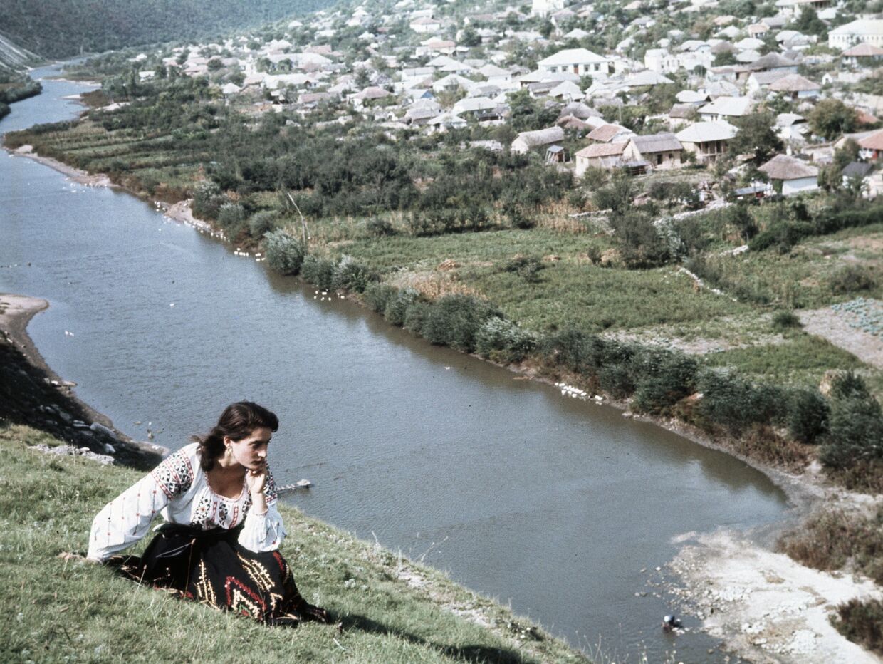 Девушка-молдаванка в национальном костюме сидит на берегу реки Реут