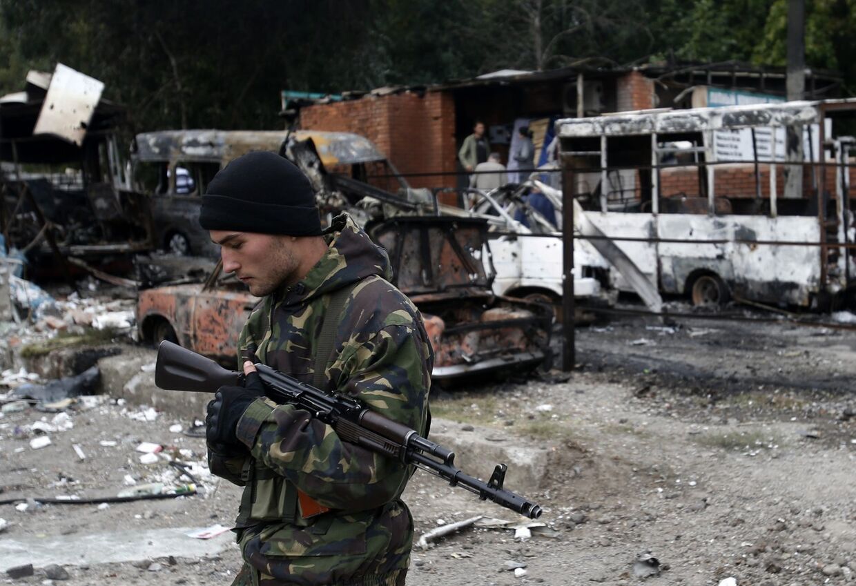 Ополченец рядом с автомобилями, поврежденными во время артобстрела Донецка
