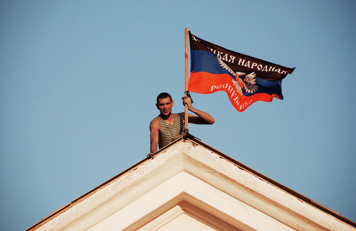 Ополченец Донецкой народной республики (ДНР) устанавливает флаг ДНР на здании мэрии города Комсомольское Донецкой области