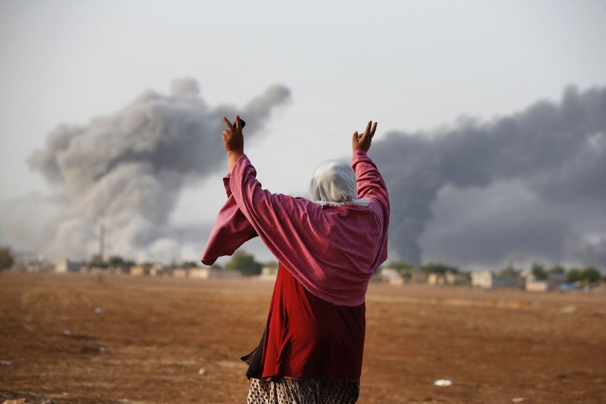 Женщина смотрит на то, как над Кобани поднимается дым после американского авиаудара 
