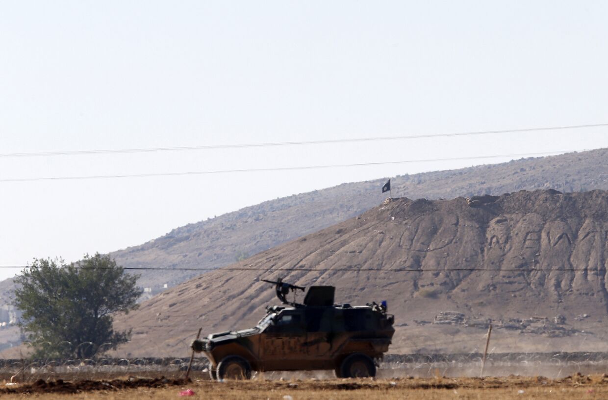 Автомобиль турецкой армии на фоне черного флага Исламского государства рядом с городом Кобани 
