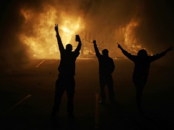 Протестующие смотрят на горящие здания магазинов
