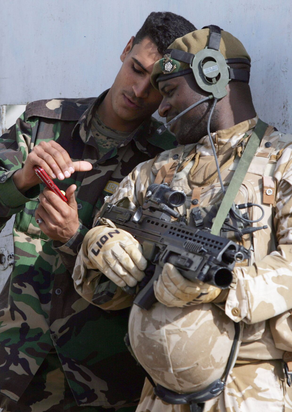Британский и иракский солдаты смотрят на экран мобильного телефона. Басра, Ирак, 2009 год