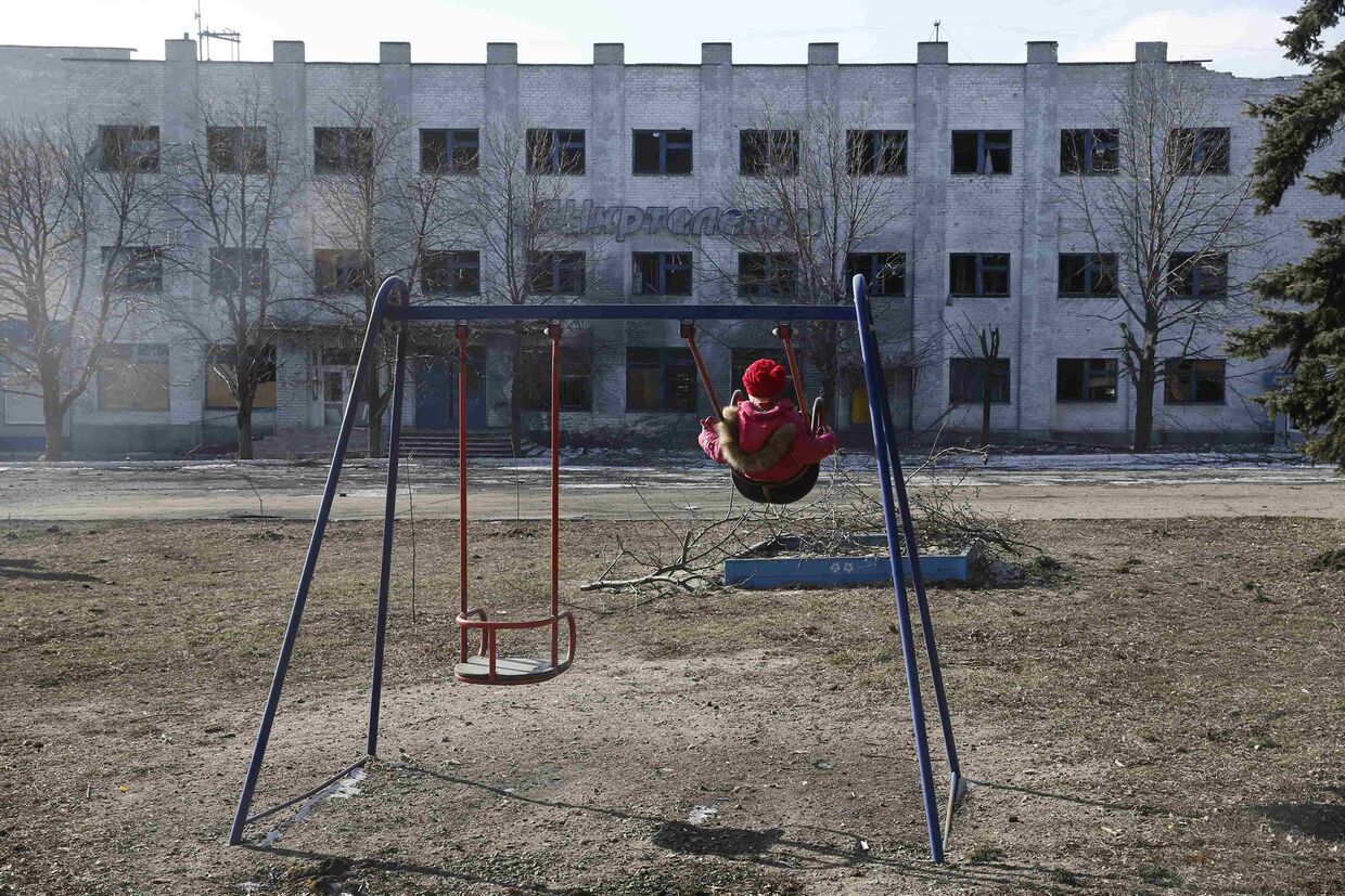 Девочка качается на качелях напротив пострадавшего во время боев здания в Дебальцево