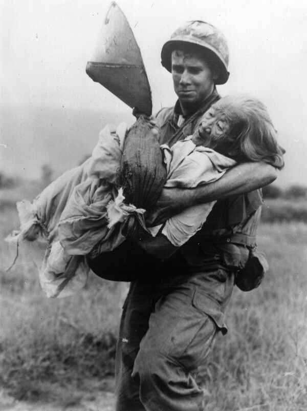 Американский солдат несет пожилую вьетнамку к вертолету для эвакуации в лагерь для беженцев