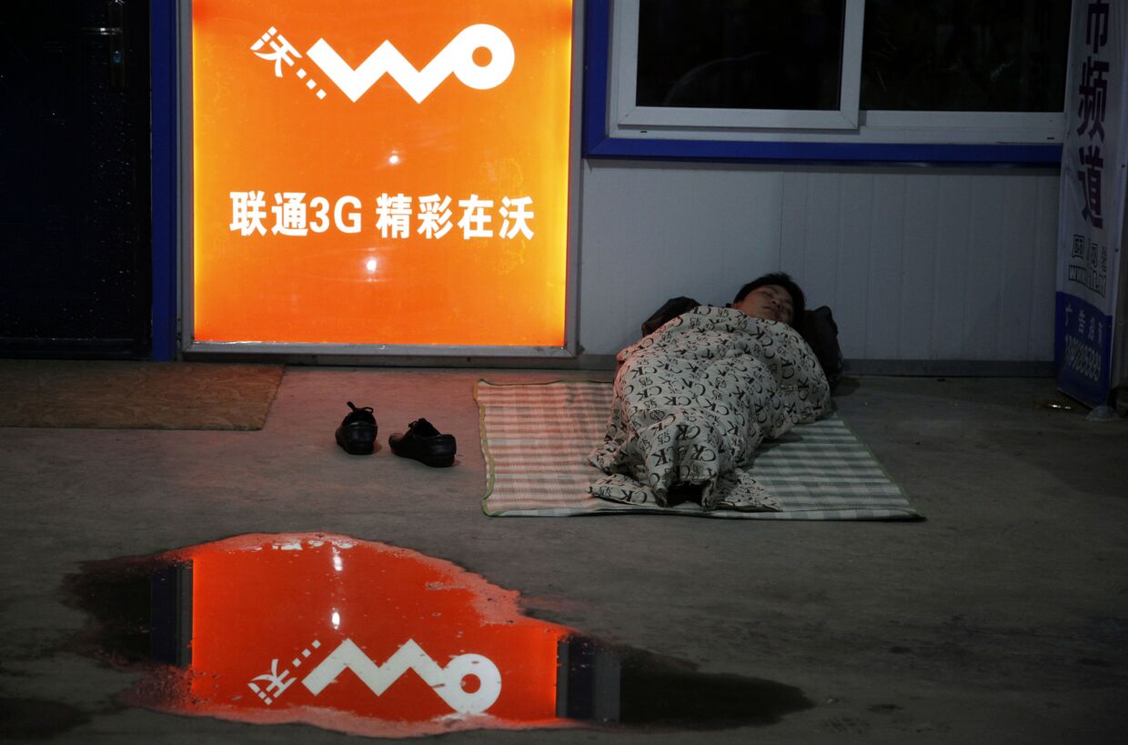 Пассажир спит на вокзале рядом с рекламой Unicom's 3G в городе Шэньян провинции Ляонин, Китай