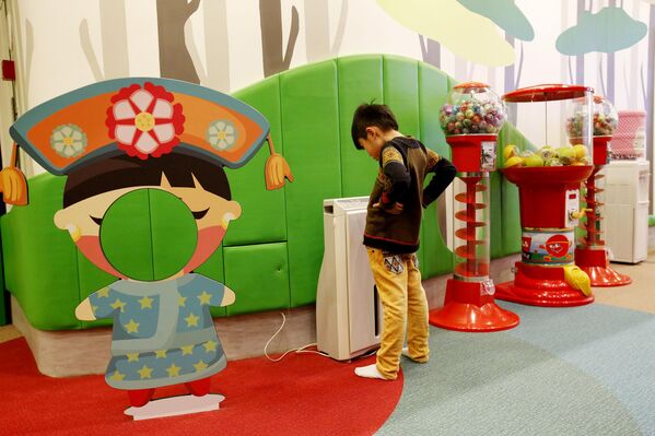 Мальчик смотрит на очиститель воздуха в игровой зоне отеля в Пекине