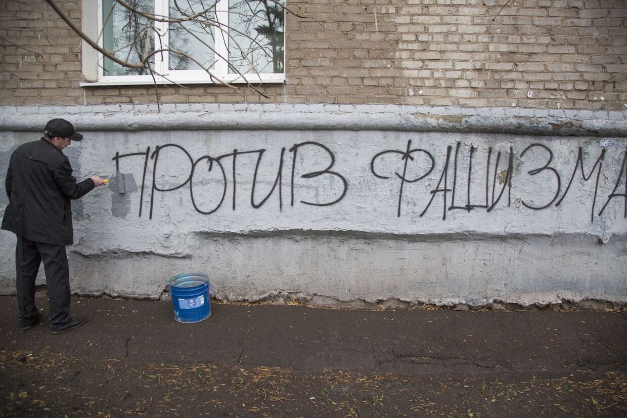Сотрудник коммунальной службы закрашивает надпись Против фашизма на стене дома по маршруту шествия Русский марш в Уфе