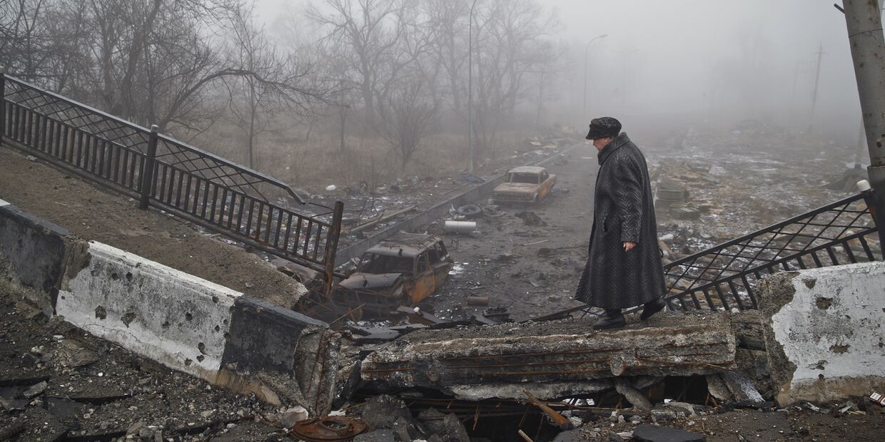 Женщина идет по полуразрушенному мосту в Донецке