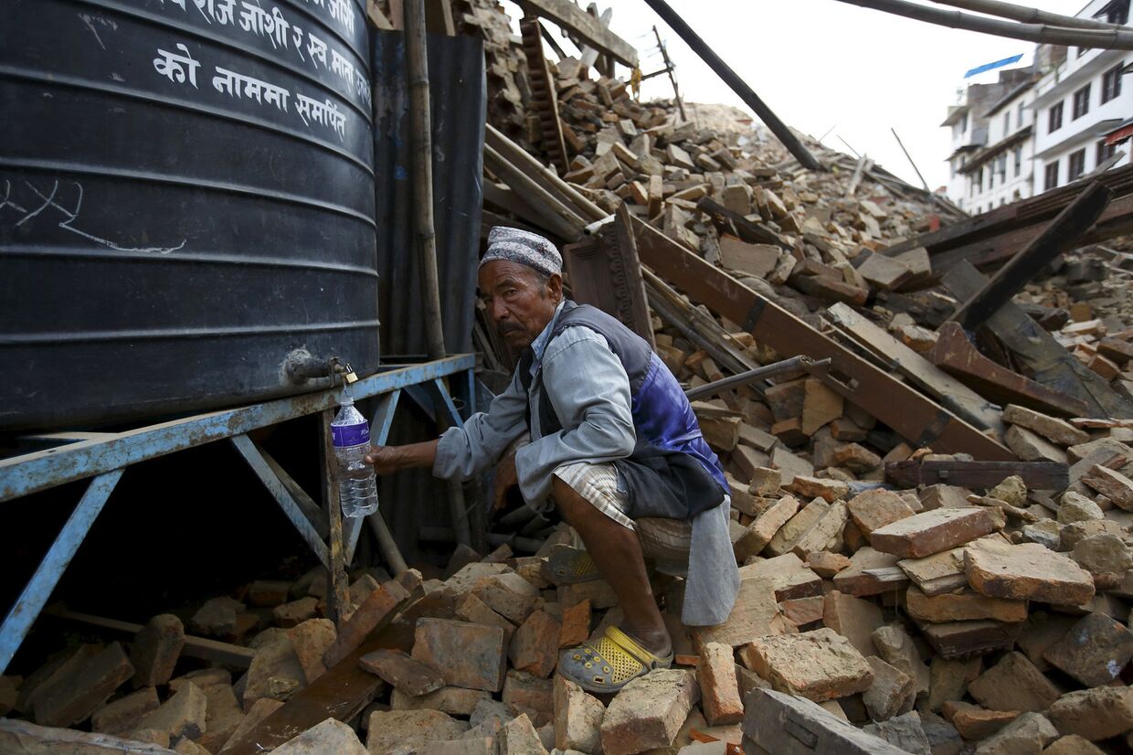 Мужчина набирает воду рядом с разрушенным храмом в Катманду