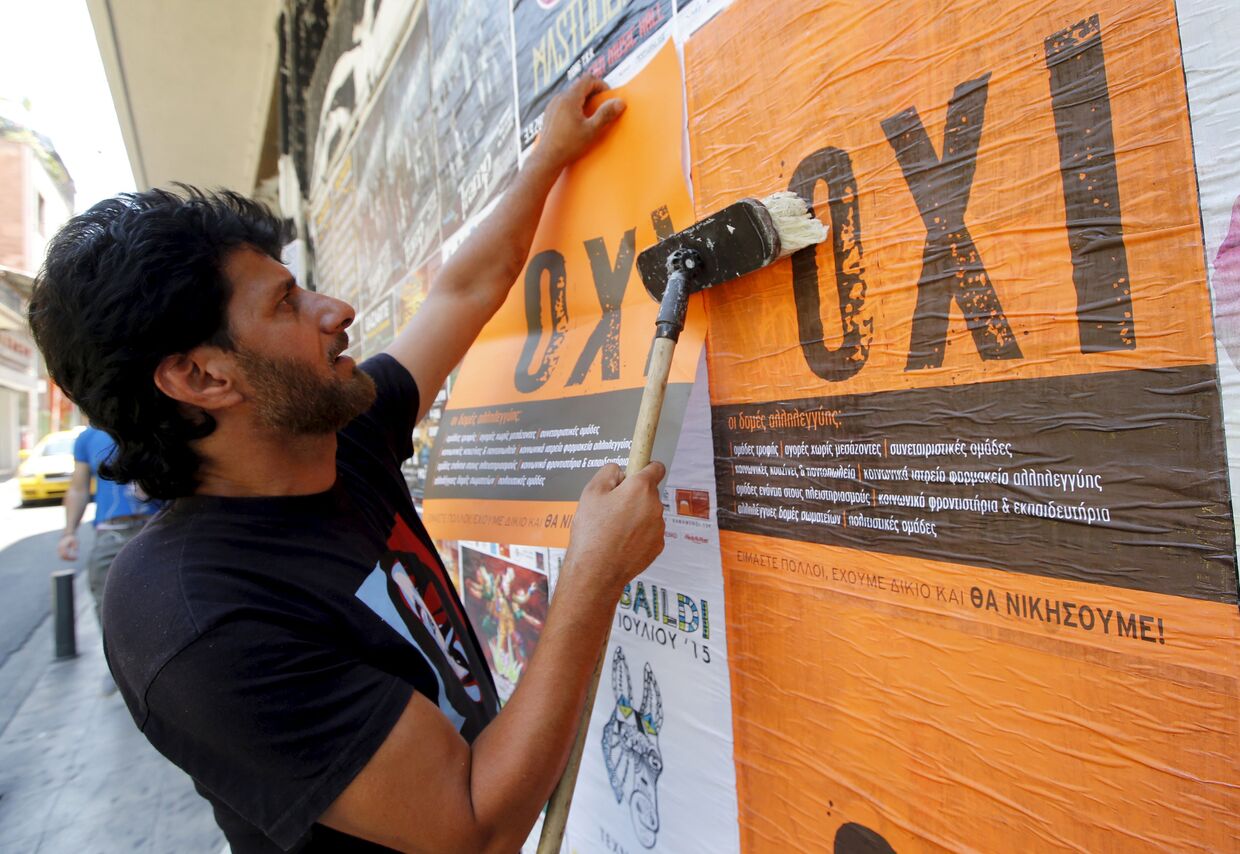 Человек клеит плакаты со словом нет по-гречески в Афинах