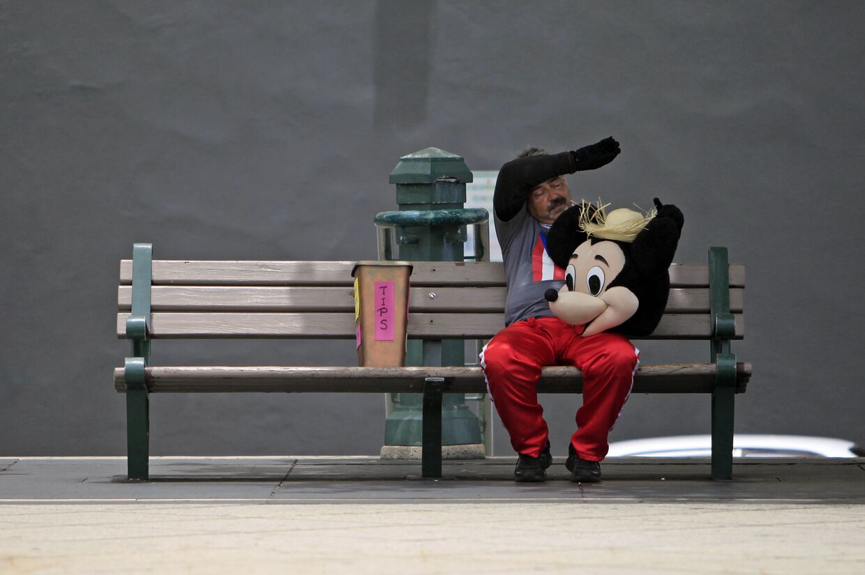 Уличный исполнитель в костюме Микки-Мауса отдыхает на скамейке в старой части Сан-Хуана, Пуэрто-Рико