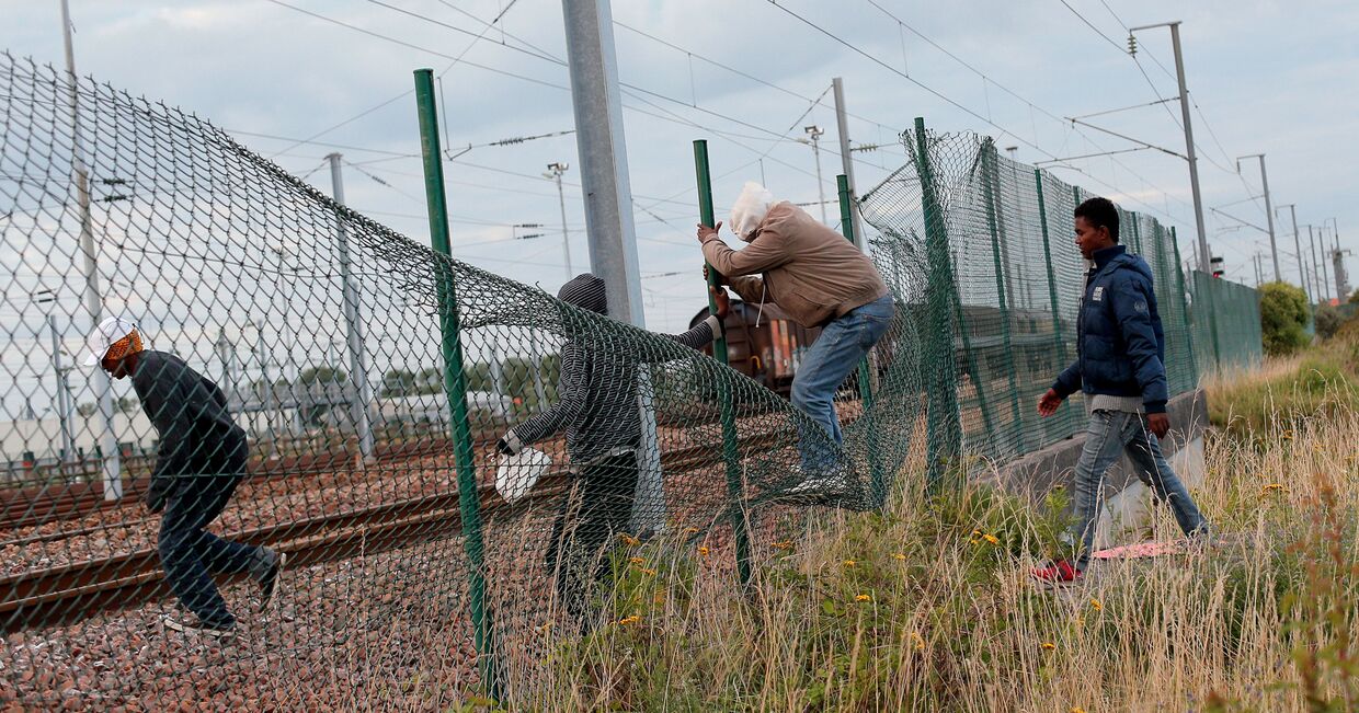 Мигранты перелезают через забор, чтобы пробраться к Евротуннелю