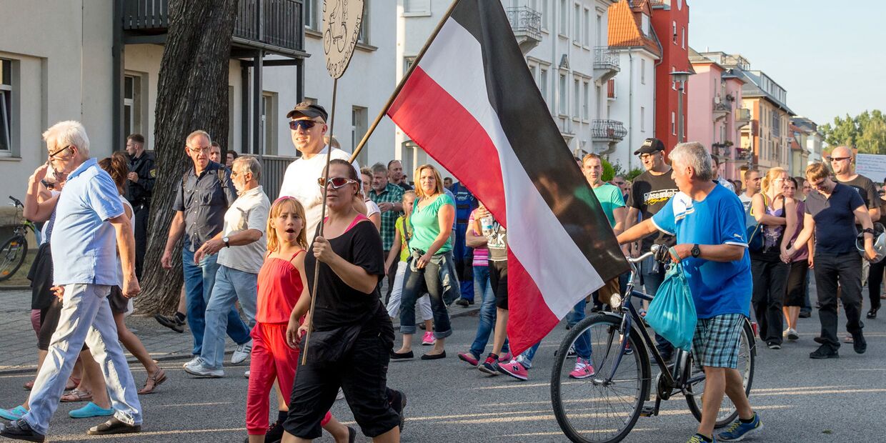 Жители Дрездена несут флаг Германской империи во время акции протеста против превращения местного рынка в приют для беженцев