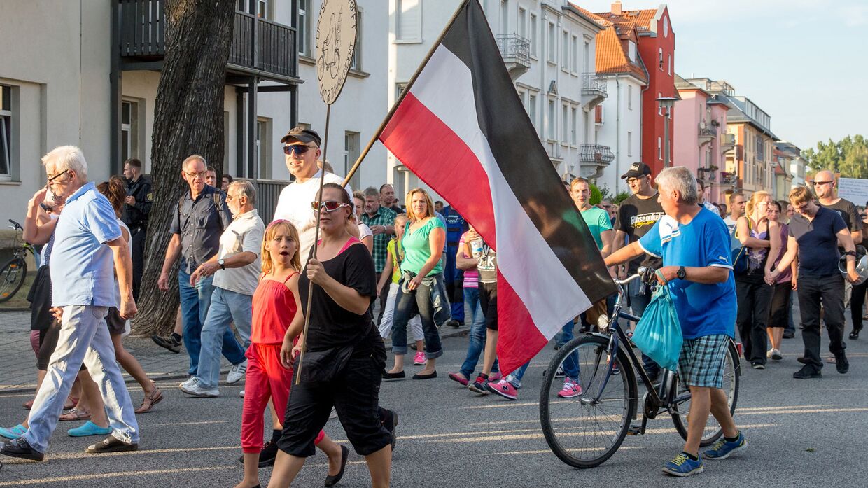 Жители Дрездена несут флаг Германской империи во время акции протеста против превращения местного рынка в приют для беженцев