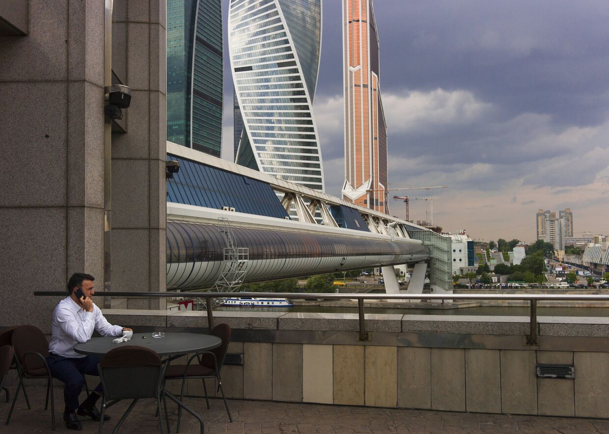 Мужчина сидит в кафе на набережной Москва-реки с видом на небоскребы «Москва-Сити»