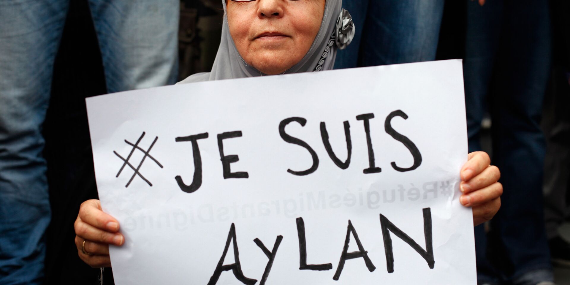 Женщина с плакатом Je suis Aylan на митинге в поддержку беженцев в Париже - ИноСМИ, 1920, 29.05.2026