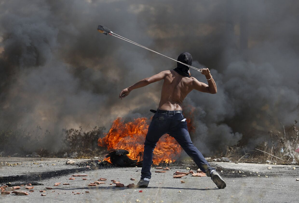 Демонстрант из Палестины бросает камни в сторону войск Израиля в ходе столкновений в Иерусалиме. Октябрь 2015