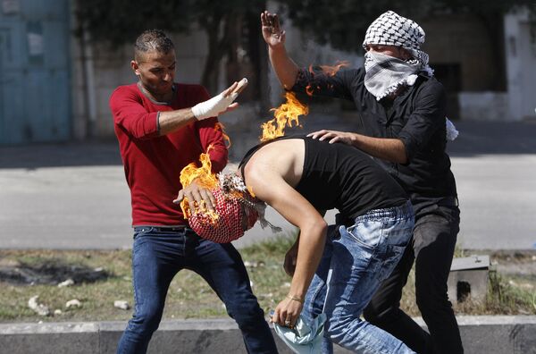 Палестинцы помогают соотечественнику сбить пламя, перекинувшееся на него из бутылки с зажигательной смесью, которую он пытался бросить в израильских полицейских
