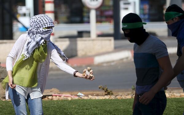 Девушка-палестинка раздает камни протестующим во время столкновений с полицией в городе Бейт-Эль