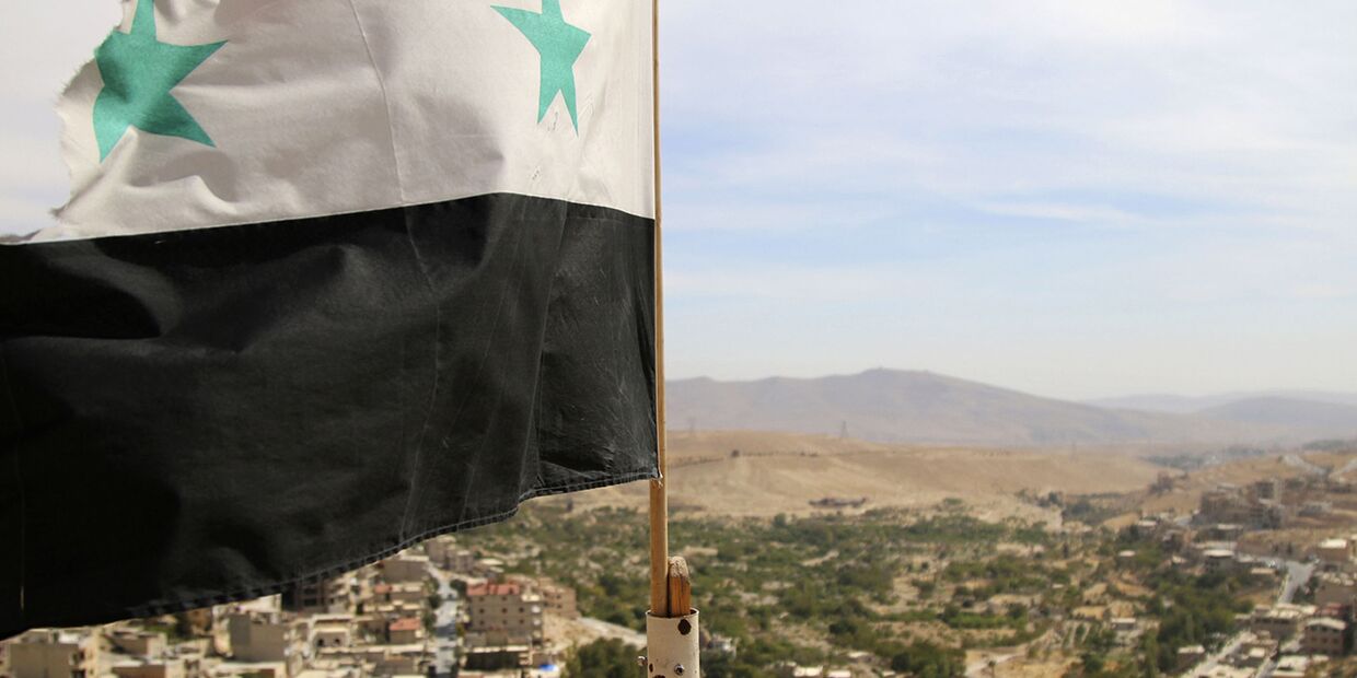 Флаг Сирии в городе Маалула к северу от Дамаска