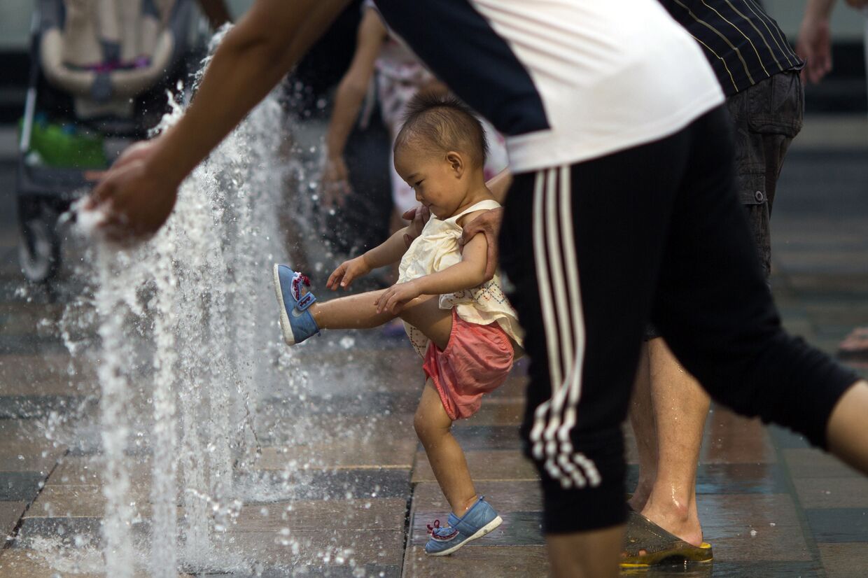 Родители играют с ребенком в фонтане у входа в торговый центре в Пекине