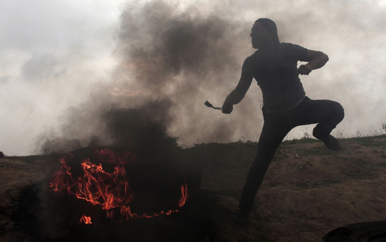 Палестинец кидает камень во время столкновений с израильскими солдатами на границе Израиля и Сектора Газа