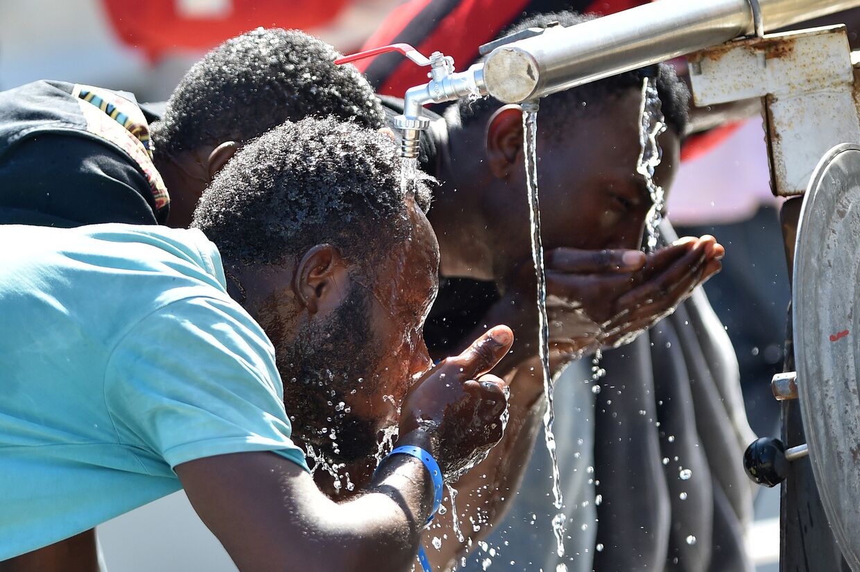 Мигранты из Африки пьют воду после прибытия на Сицилию