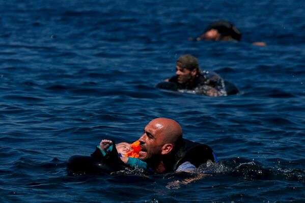 Беженец с ребенком плывет к острову Лесбос после кораблекрушения
