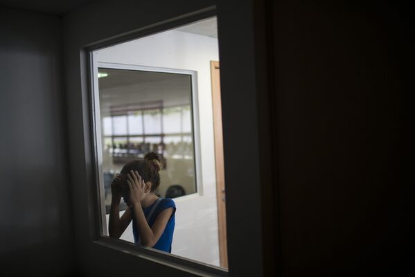 Дженнифер Карине смотрит в помещение, где ее брат Хуан Педро, рожденный с микроцефалией проходит обследование