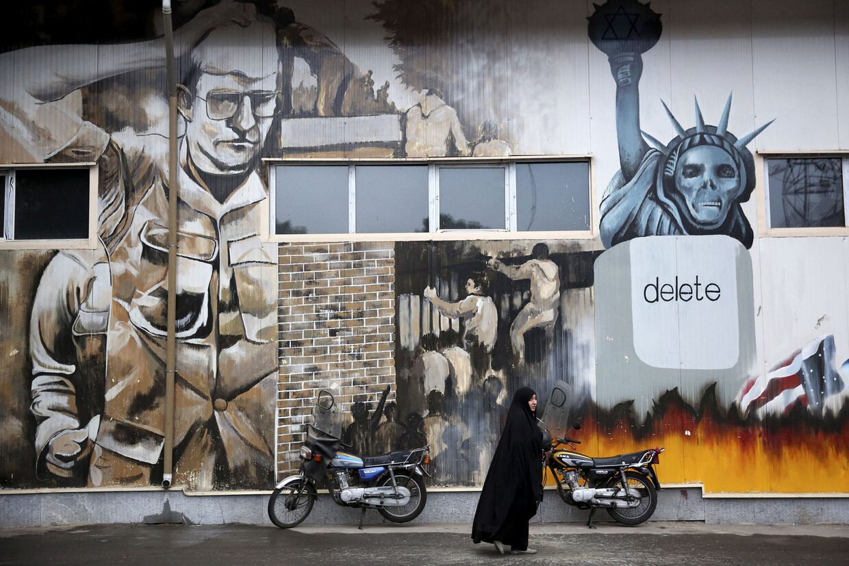 Женщина на фоне граффити на стенах бывшего посольства США в Тегеране, Иран