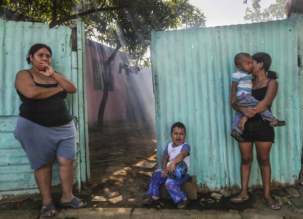 Женщины с детьми ждут пока их дом обработают инсектицидами против комаров вида Аedes Аegypti, переносящих вирус Зика