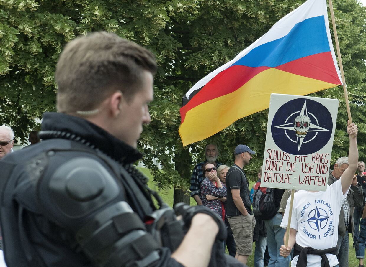 Митингующий держит в руках выдуманный Русско-Германский флаг на митинге против мигрантов