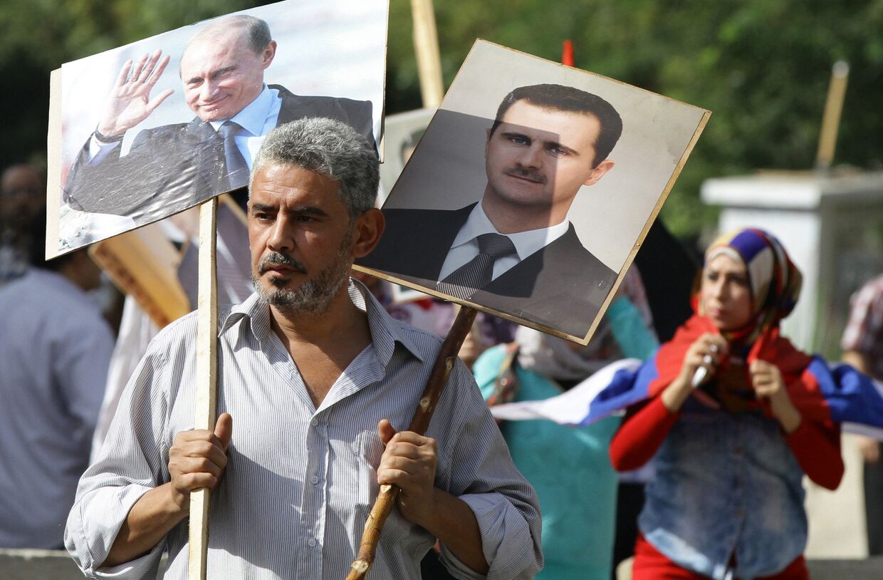 Сириец держит плакаты с изображениями Владимира Путина и Башара Асада на акции в поддержку российских военных действий в Сирии, Дамаск