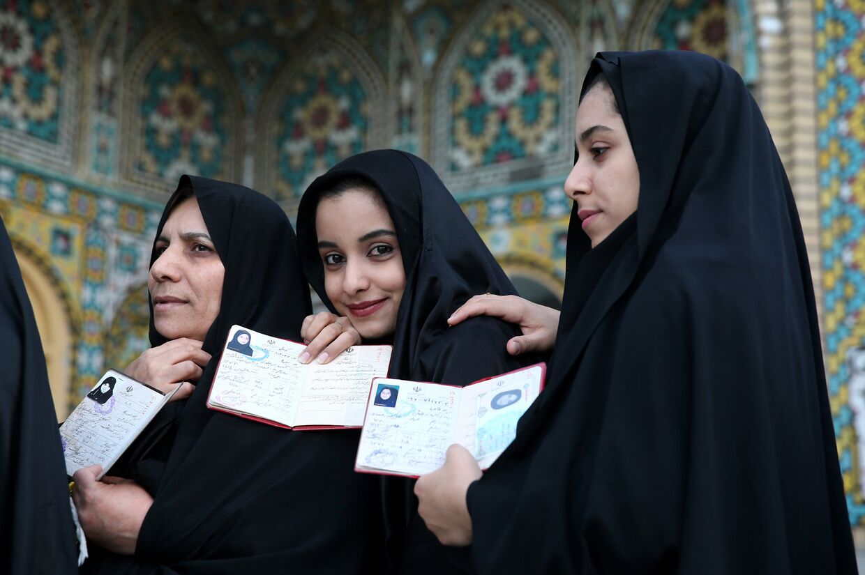 Иранские девушки показывают паспорта на избирательном участке на выборах в парламент и в совет религиозных экспертов в Иране