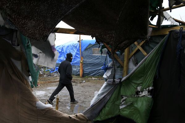 Житель лагеря эмигрантов Джунгли, недалеко от Кале идет мимо разрушенных палаток