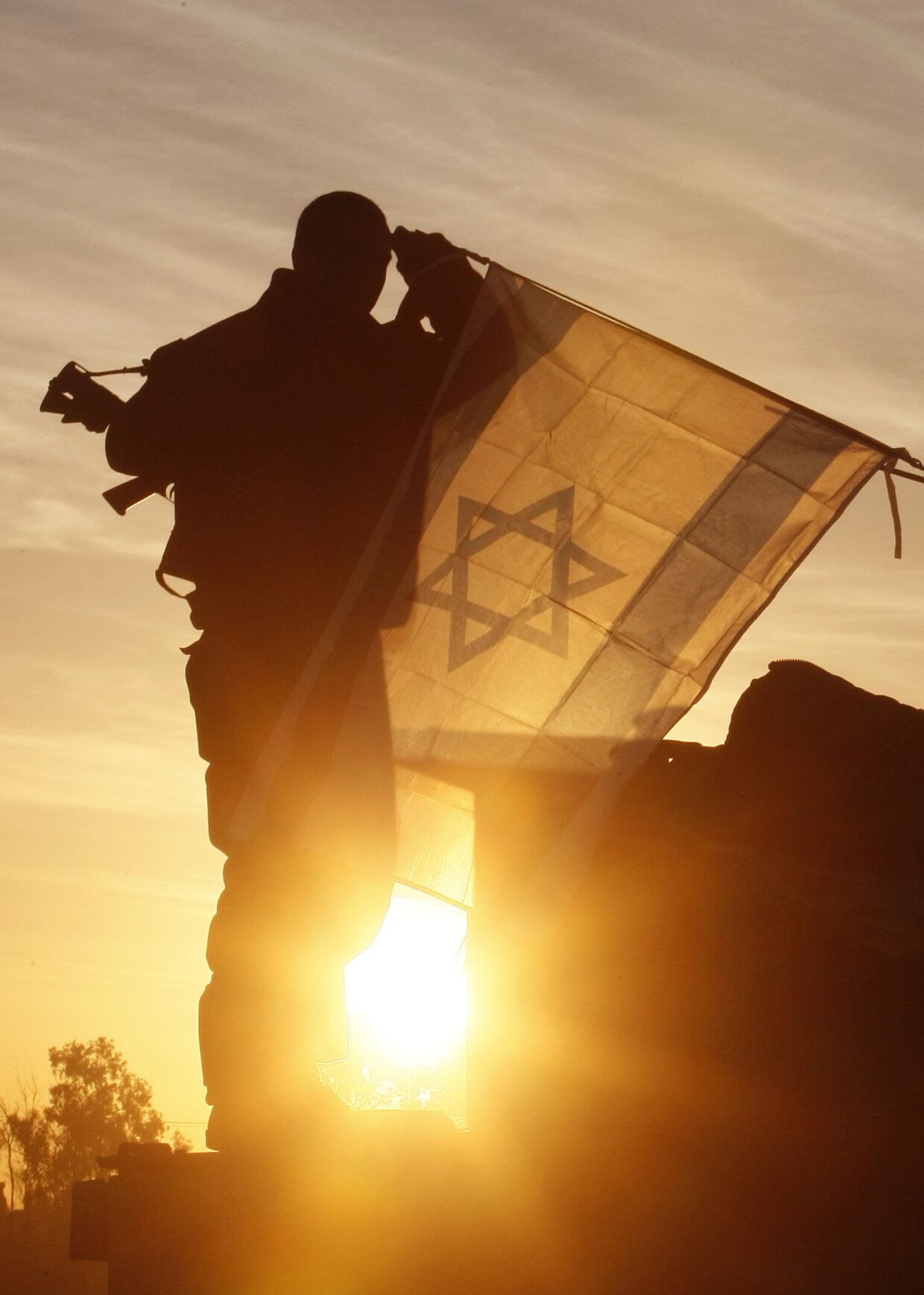 Солдат армии Израиля вешает государственный флаг на танк на израильской стороне границы