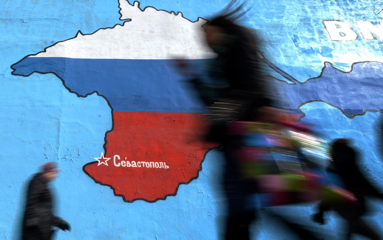 Прохожие у нарисованной на стене карты Крыма в цветах российского флага в Москве