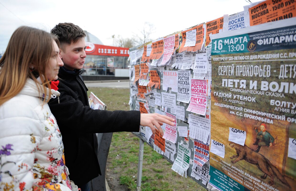 Юные жители города читают объявления на уличном стенде в Донецке