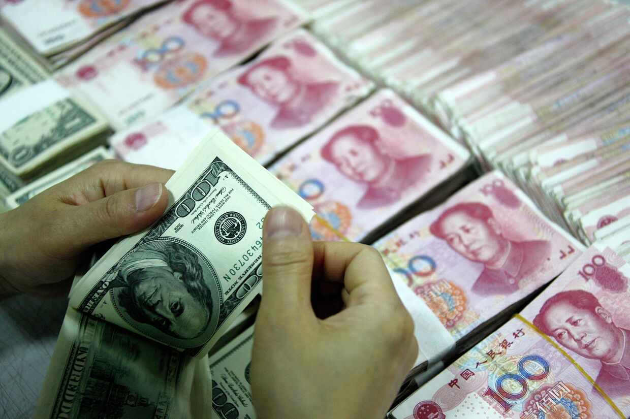 Банковский служащий пересчитывает доллары рядом с пачками юаней в городе Хуайбэй, Китай