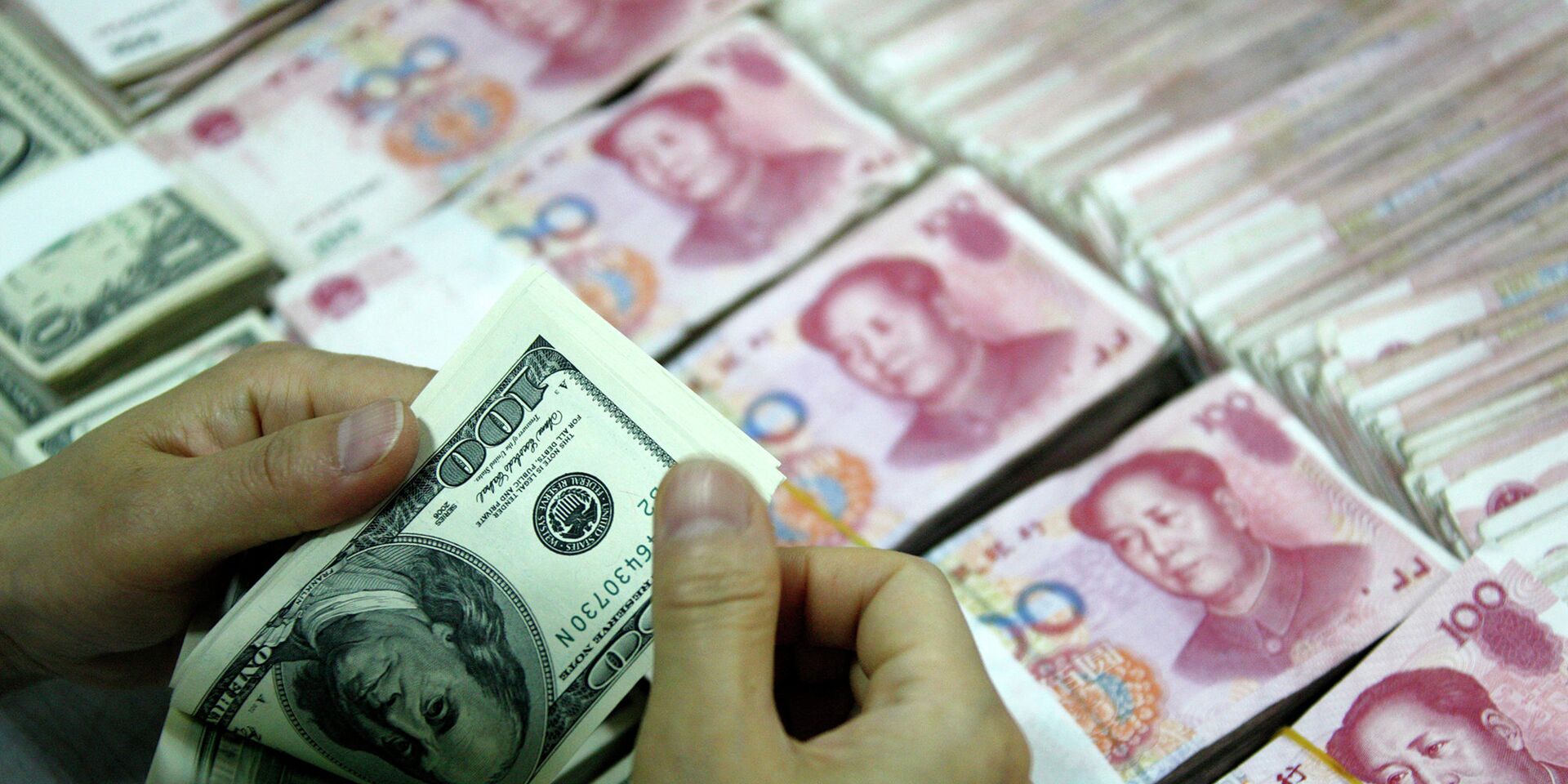 Банковский служащий пересчитывает доллары рядом с пачками юаней в городе Хуайбэй, Китай - ИноСМИ, 1920, 30.01.2024