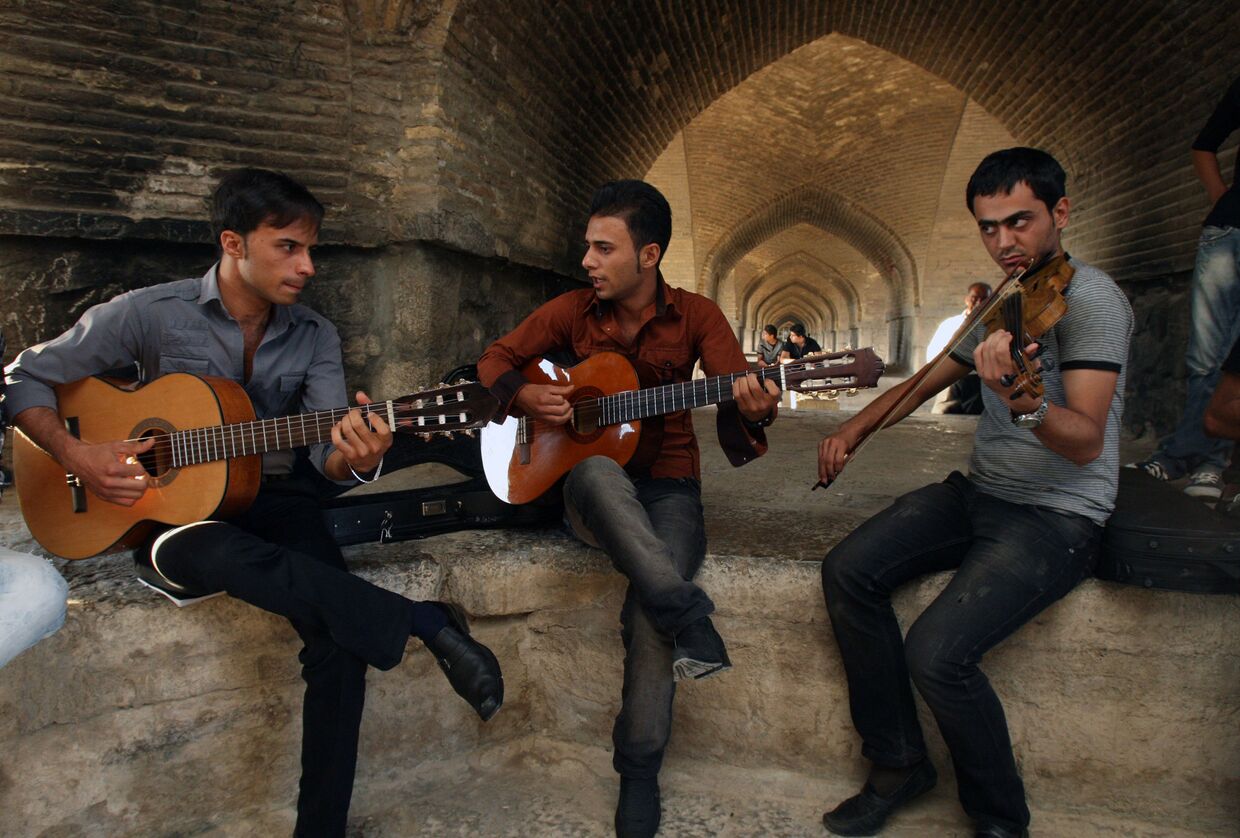 Молодые люди играют на музыкальных инструментах рядом с Мостом 33 арок в Исфахане
