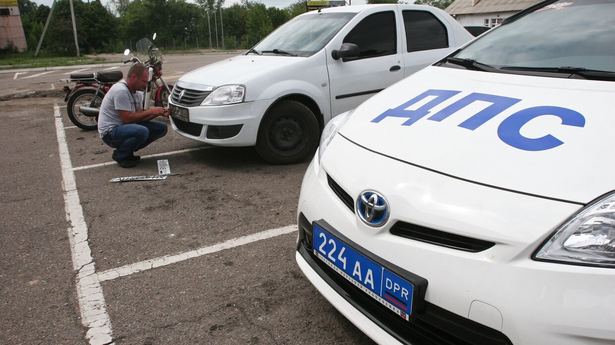 Мужчина устанавливает номерной регистрационный знак Донецкой народной республики на автомобиль в Донецке