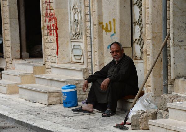 Мужчина сидит на крыльце дома на одной из улиц Пальмиры