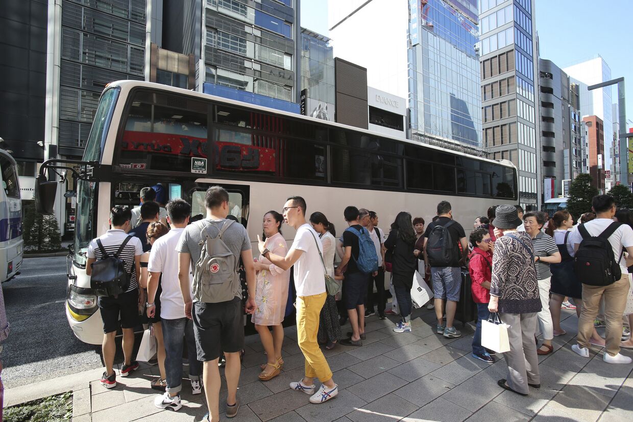 Китайские туристы ждут в очереди в автобус в Токио